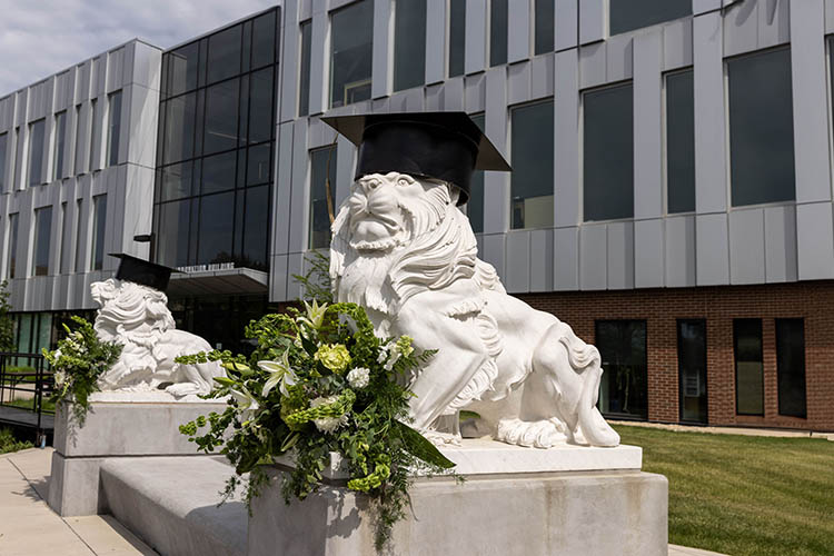 Two white lion statues wearing graduation caps outside of Hammond’s Nils building. The statues are decorated with white and green floral arrangements.