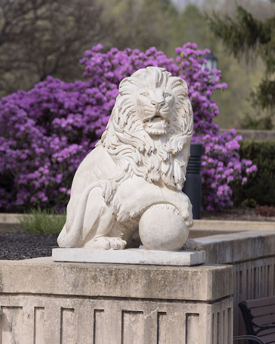 A white lion statue on the PNW Westville Campus it. There is a purple flowering plant in the background.