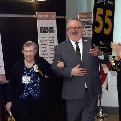PNW Chancellor Chris Holford escorts 55 years of service honoree Shelia Rezak through the crowd.