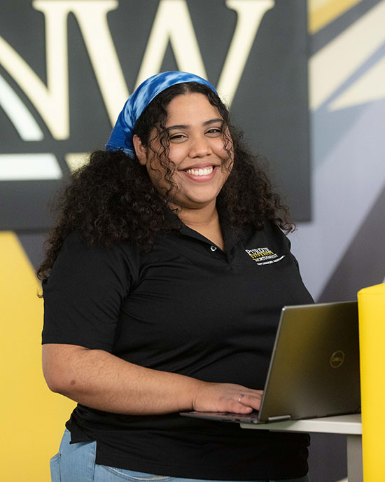 A PNW student standing and working at a laptop.