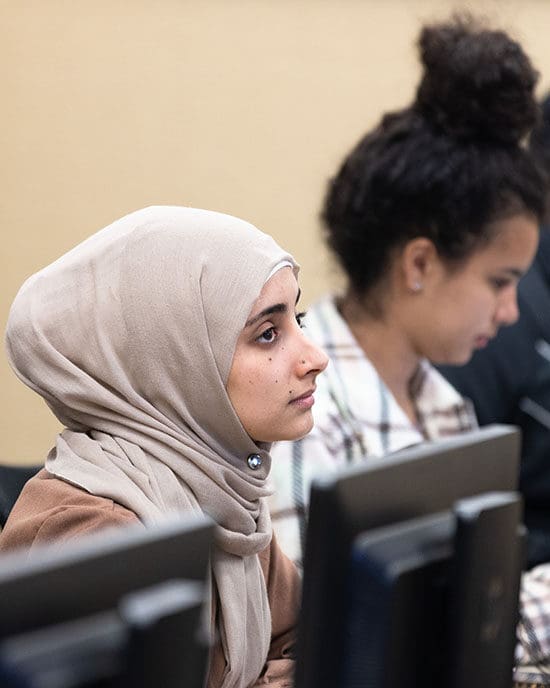 Two students sit at desktop computers.