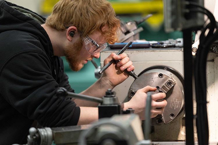 Students on the Baja motorsports team works with a tool on a machine