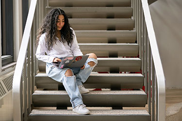 A PNW student reads a laptop on a stairway