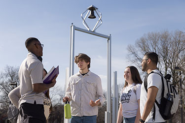 Five students stand outdoors. The PNW Belltower is in the background