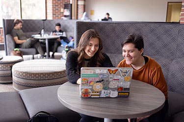 Students work over a laptop in a PNW lounge