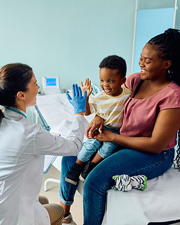 Happy African American boy giving high five to his pediatrician after medical examination at doctor's office.