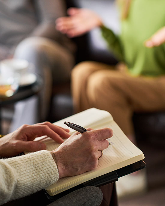 Vertical shot of adult couple attending therapy session, female therapist taking notes while woman speaking, conveying relationship counseling and mental health support.
