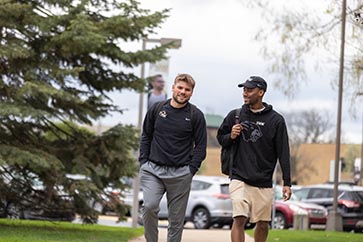 Two PNW students walking and talking on campus 363x242