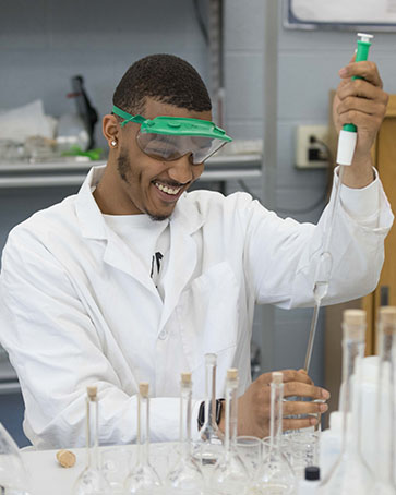 A student in a white labcoat uses a syringe to put liquid in a test tube