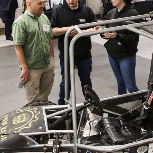 Students stand around a baja team car.