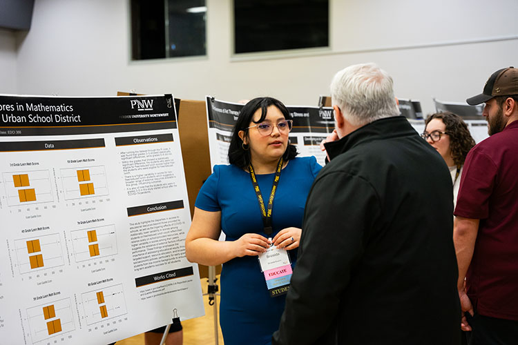 People are engaged in conversation while examining a research poster at Days of Discovery