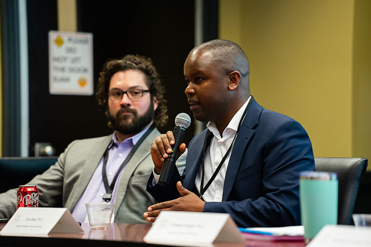Ezra Mutai sits at a table and speaks into a hand-held microphone.