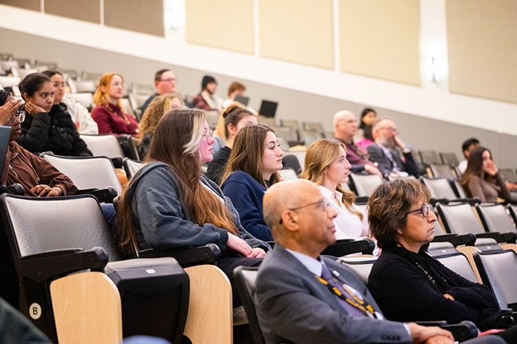 Faculty, staff and students sit in a lecture style classroom