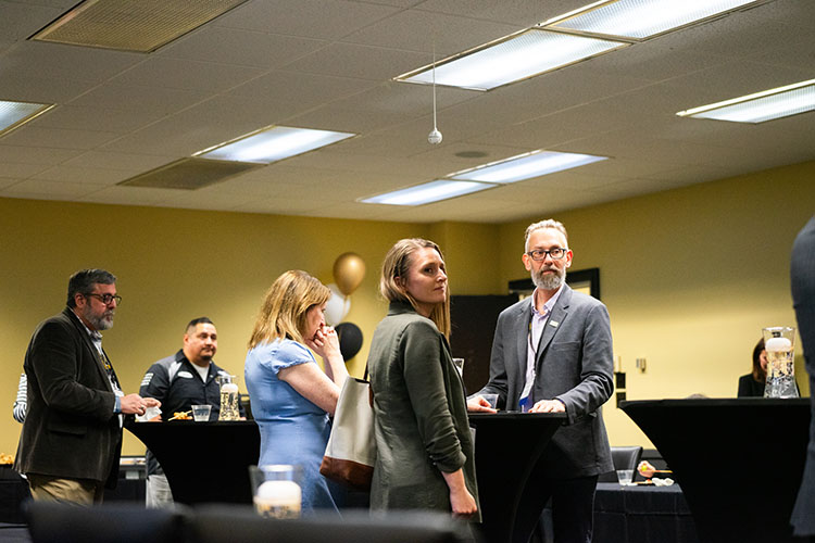 A group of faculty and staff stand in a room with high tables, conference materials and refreshments during days of discovery