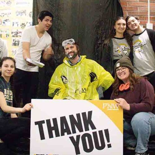 Six people pose together behind a PNW branded "Thank You" sign