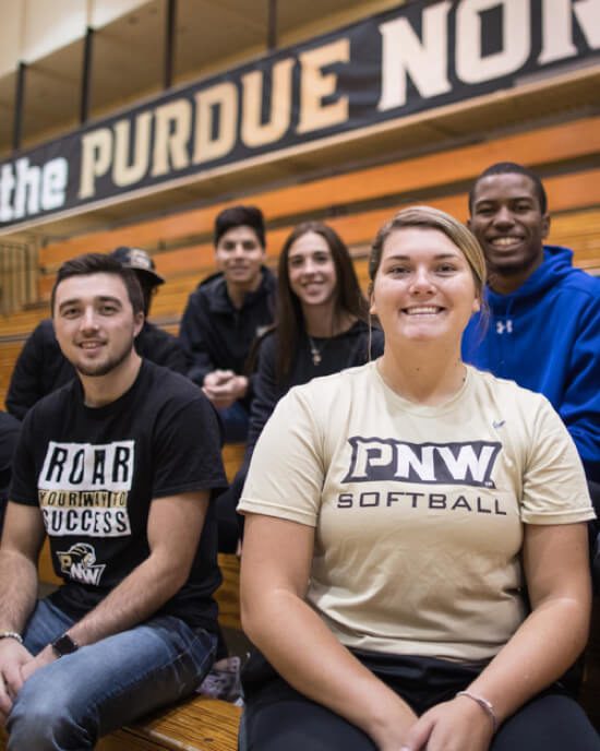 PNW students pose together in a gym, with one wearing a PNW softball shirt.