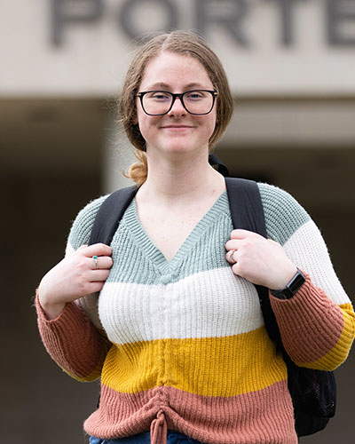 A PNW student in a sweater stands outdoors