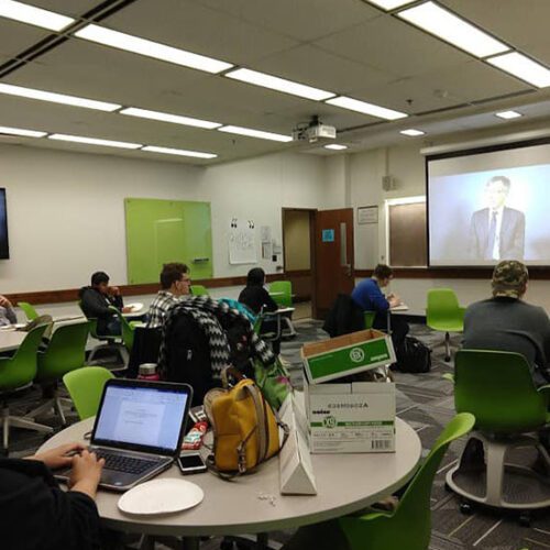 Students sit in a classroom watching a video being projected onto a screen