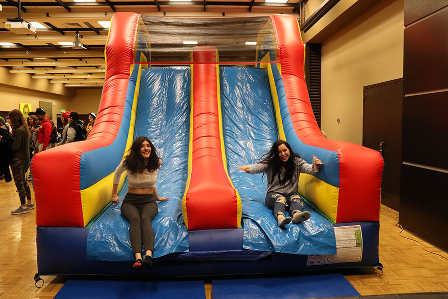 Two students slide down an inflatable slide in Alumni Hall