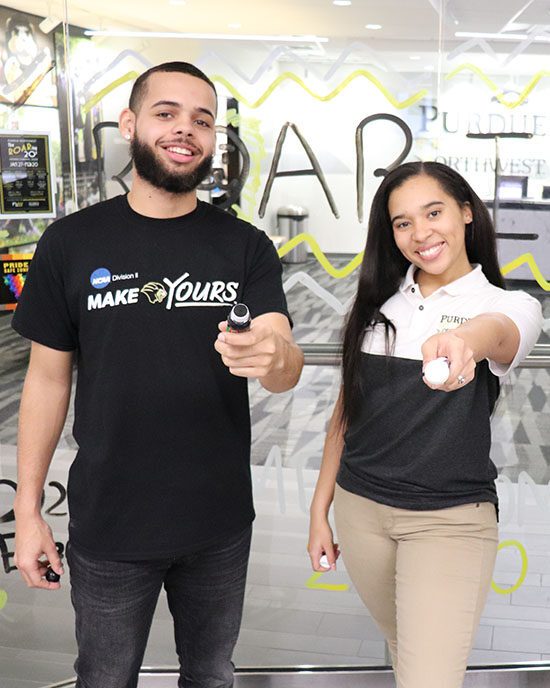 Two students pose with window markers in front of a window painting they did for homecoming