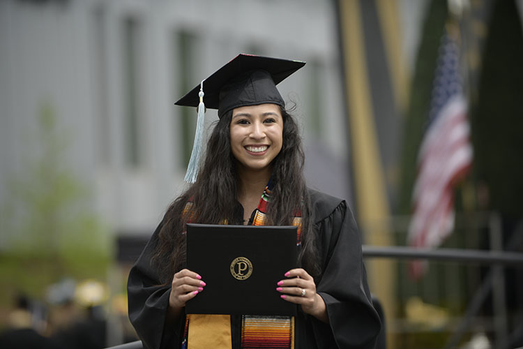 A student in a cap and gown poses with her diploma