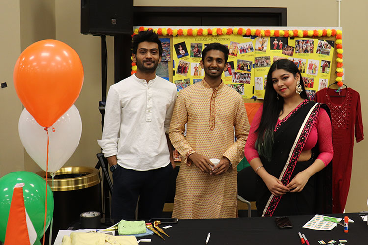 Three students pose together behind a table