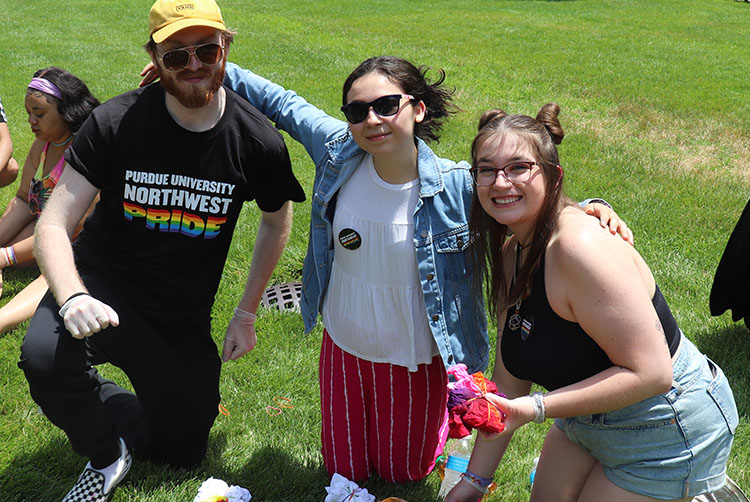 Three students pose together outdoors while tie dying shirts