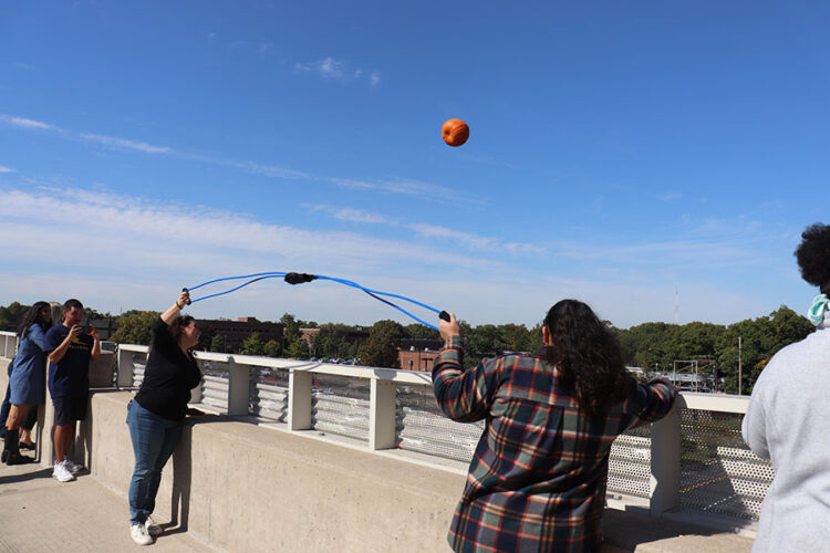 Two students hold a catapult while a pumpkin flies through the air