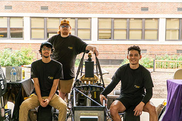 Three students in the Baja club sit around the club's car.