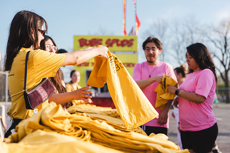 Four students stand around a table that is piled with bright gold t-shirts