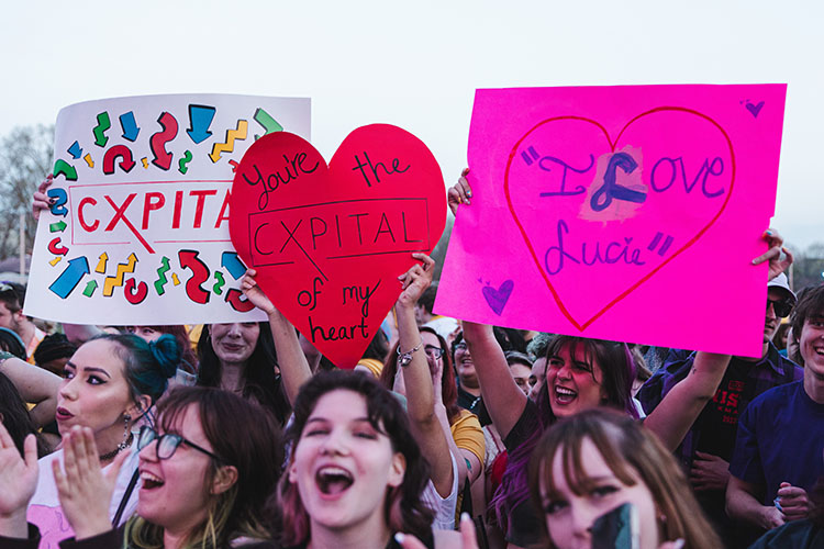 Students in the crowd hold up homemade signs during the Cxpital performance