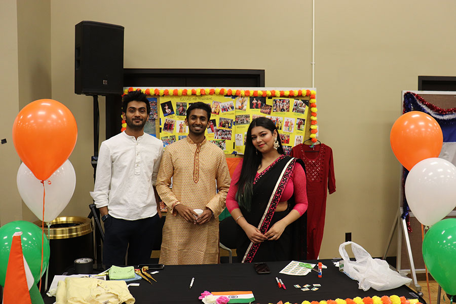 Three students stand in traditional Indian attire behind an Indian themed table during the Global Groove event.
