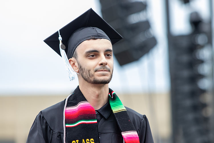 A first-generation PNW student showing off a silver cord at commencement