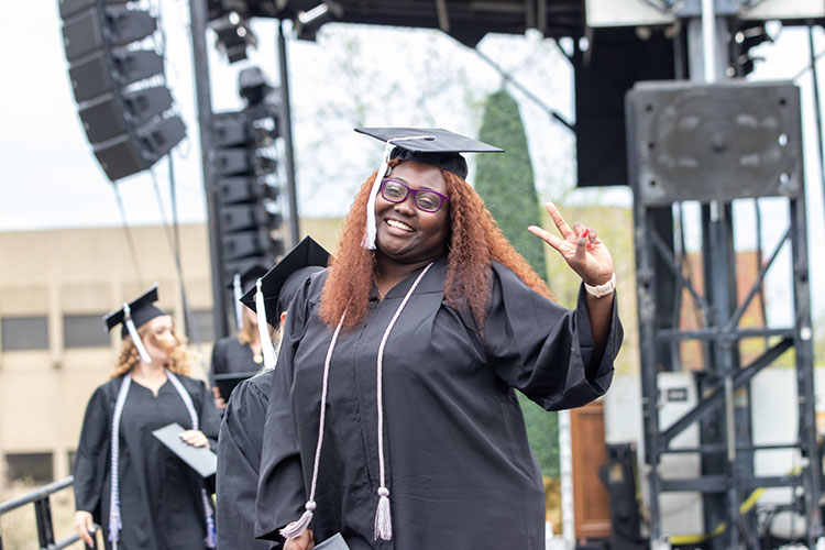 A first-generation PNW student showing off a silver cord at commencement