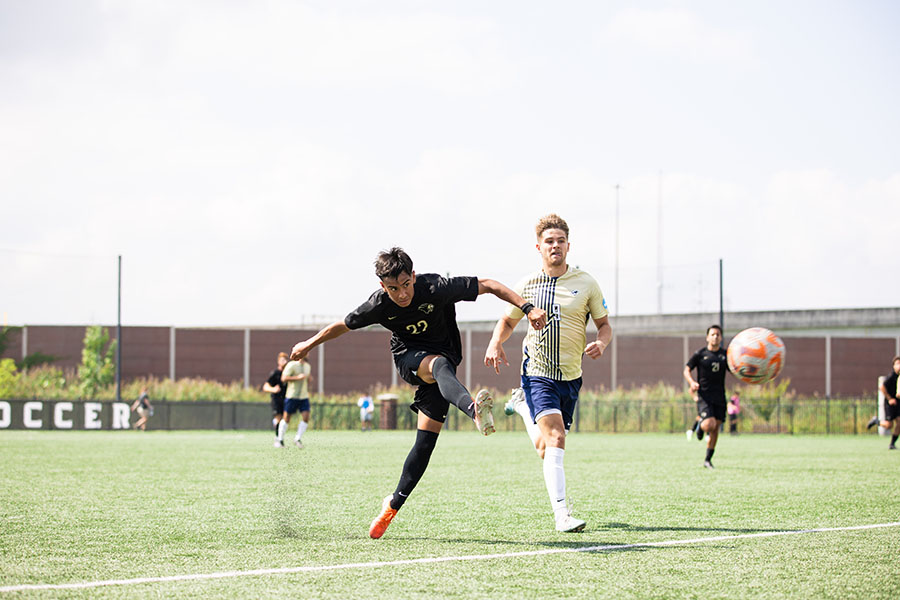 Two men's soccer players run downfield. The ball is in mid-air