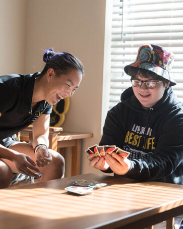 Two students sit at a table. They are playing Uno.