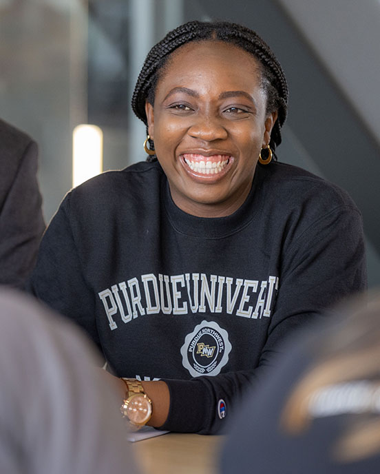 A student in a black "PNW" sweatshirt sits at a table and smiles.