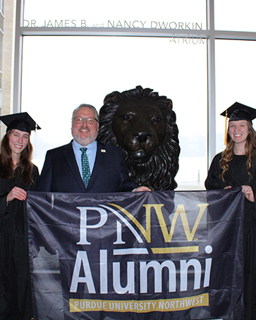 Chancellor with two graduates holding an alumni sign