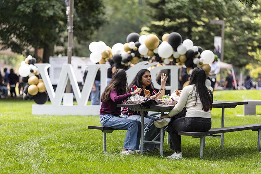3 students eating at a picnic table with the PNW sign in the background