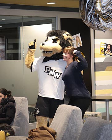 PNW student posing with Leo the Lion mascot in the Mane Zone