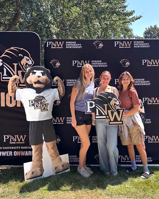 PNW students at the Hammond Welcome Rally pose with a PNW sign next to a cardboard cutout of mascot Leo.