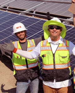 Technicians pose with arms outstretched at a solar-panel site.