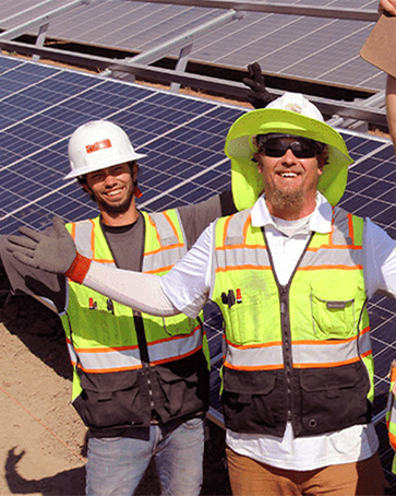 Technicians pose with arms outstretched at a solar-panel site.
