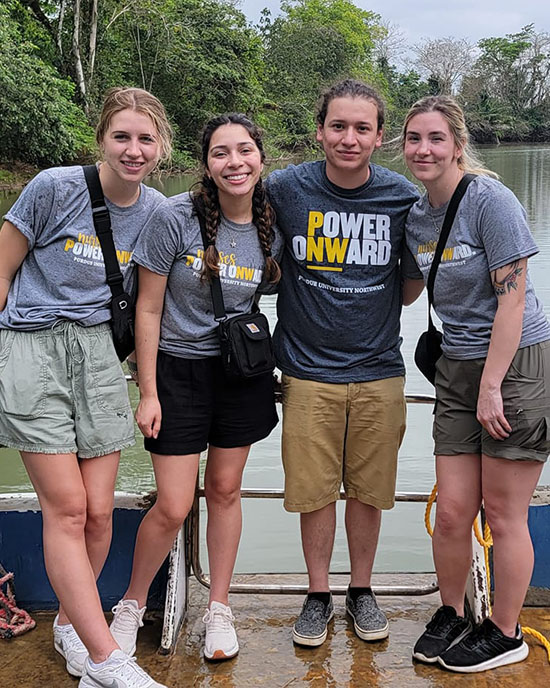 Four students in PNW Nursing shirts stand at the edge of a boat
