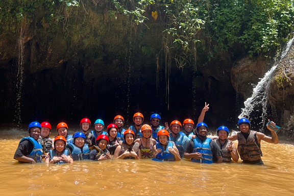 Students on a study away trip stand in a river in helmets and life jackets