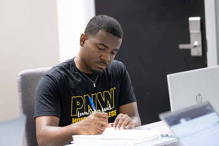 A student sits at a table and writes on a piece of paper