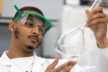A student in a lab coat inspects a flask.