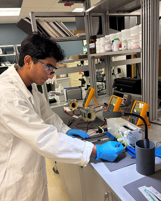 A PNW student in a white lab coat works with a water sample.