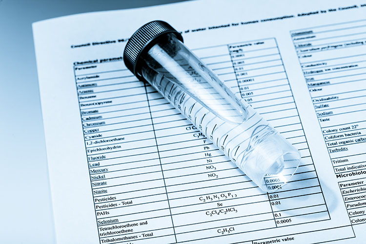 a test tube filled with water sits on paper that is printed with test results.