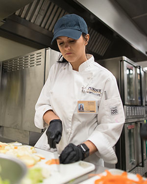 Student stands in a kitchen and chops vegetables